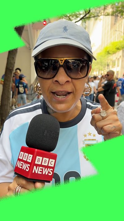A woman wearing an Argentina shirt and sunglasses points her index finger to the camera