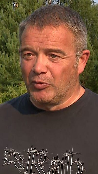 Man with grey hair, tanned skin and dark Rab top on