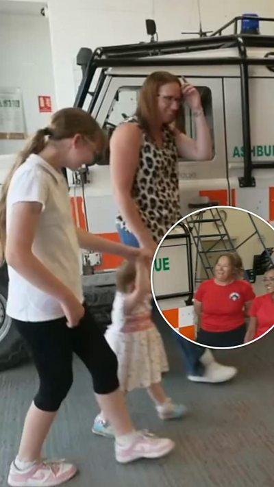 A woman and two children walking past a rescue team landrover