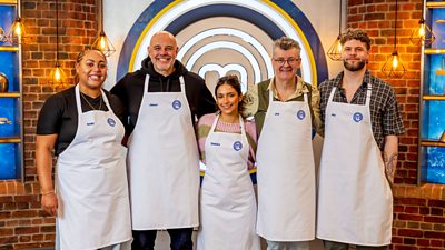 The group of five masterchef contestants wearing white aprons standing in a line and smiling towards the camera