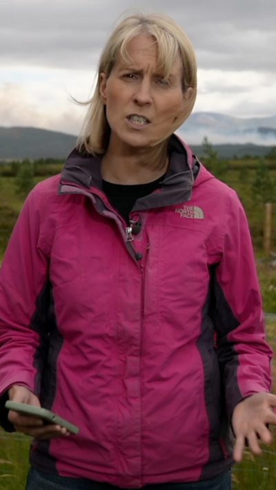 Katie Hunter wearing a pink windproof coat, as she speaks to camera in front of a cloudy sky.