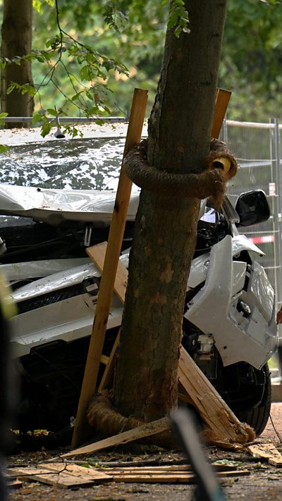 A white van with a bent bonnet up against a tree