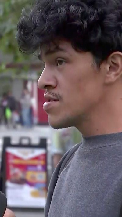 A man in a grey t-shirt with dark curly hair is seen in profile.