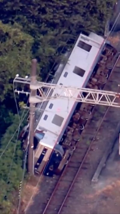 A train locomotive lays on its side beside the railway track.