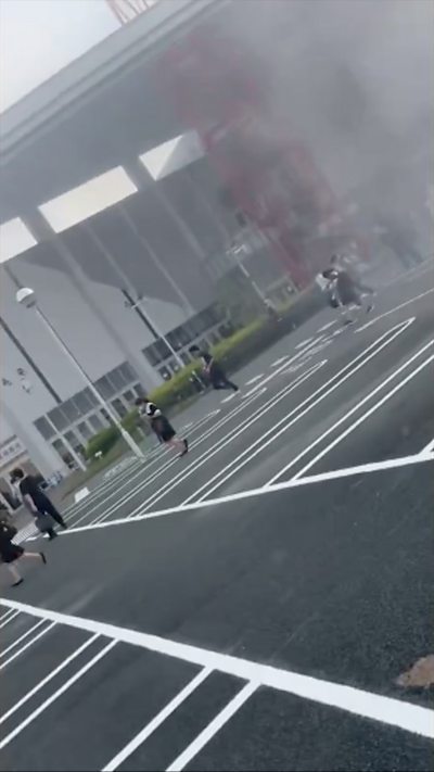 People flee from a building with smoke rising in the background