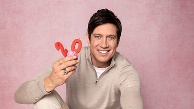 Vernon kay smiling holding a cupcake with 20th birthday candles on it