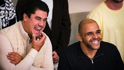 Two men sat in a crowd smiling and laughing
