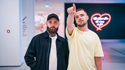  Gavin and Liam stood in a gallery as one points to something behind the camera