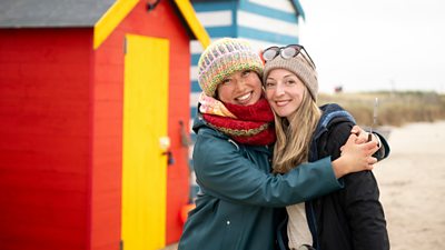 Athena Cauley Yu with Rachel Stubbs hugging and smiling in front of a red and yellow beach hut