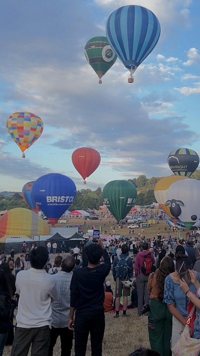 Hot air balloons with a blue sky background and people watching taking photos.