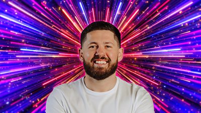 Headshot of John Nellis in front of branding for Strictly Come Dancing 2026 - a background of glittering pink, purple and gold beams of light.