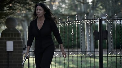 Scene from This City is Ours series 2. Elaine (Julie Graham) walks away from a graveyard wearing a long, black dress and carrying a handgun. 