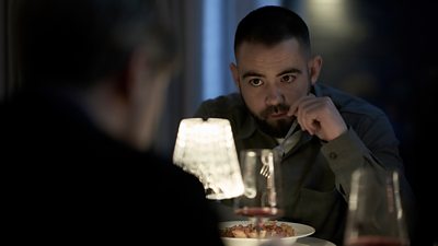 Scene from This City is Ours series 2. Close-up of Jamie (Jack McMullen) sat at a small table in a restaurant. A lamp in the middle of the table illuminates him eating a bowl of pasta. An unidentified figure sits opposite him. 