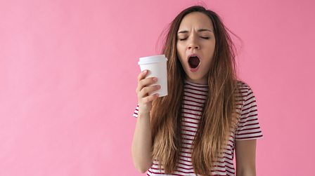 Girl holding a cup of coffee and yawning
