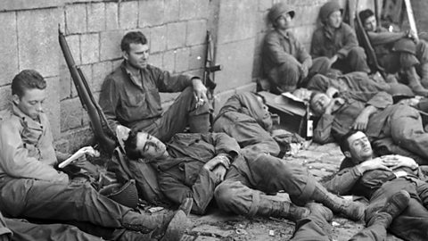 Soldiers leaning against a wall, looking exhausted. 