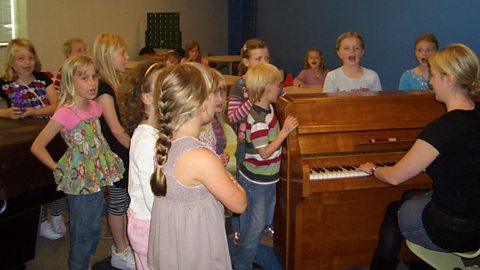 A group of children singing near a piano