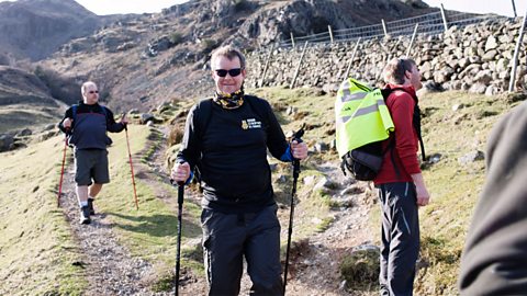 A man wearing a Children in Need jumper holding walking sticks