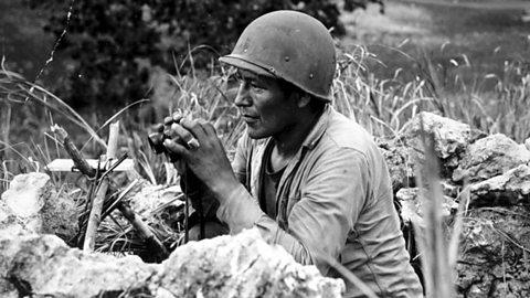 A code talker in a battle, crouching and using binoculars.  