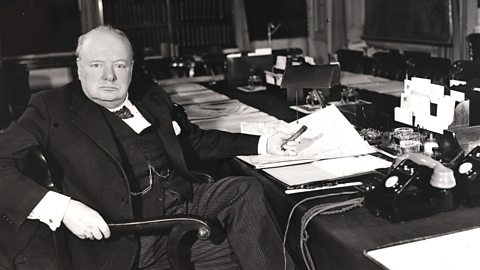 Winston Churchill sitting at a desk with some papers