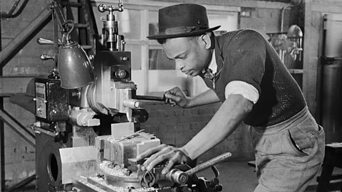 A Caribbean man working at a machine in a munitions factory