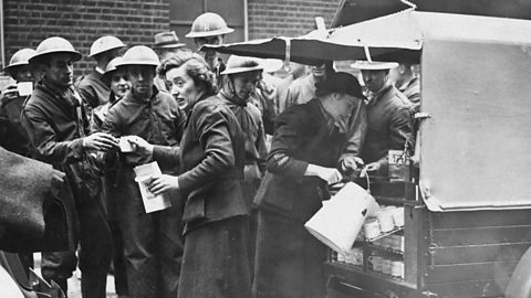 A woman serving soldiers tea from the back of a truck