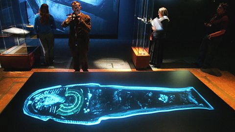 A modern exhibition of Tutankhamun, showing vistors photographing a neon outline of Tutankhamuns coffin.