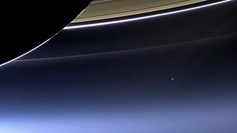 The pale blue dot of Earth below the rings of Saturn.