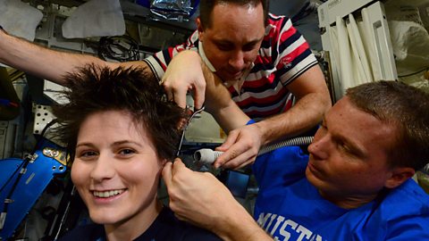 Crew members on the ISS give a fellow astronaut a haircut using scissors and a vacuum.