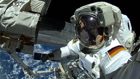 An astronaut outside the ISS with the backdrop of Earth surrounded by space.