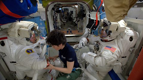 Astronaut Samantha Cristoforetti helps two fellow crew member dress for a spacewalk.