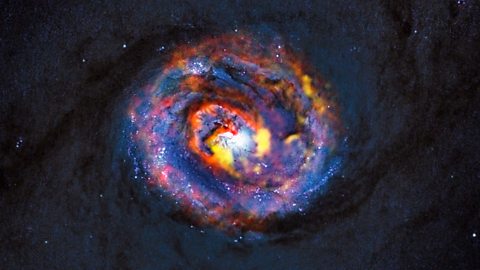 This image combines data from two telescopes. The dim background image, showing the central dust lanes of a galaxy, was captured by the Hubble Space Telescope. The central coloured structures were made by the high-altitude radio telescope ALMA.