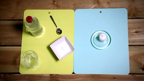 An image showing vinegar, bicarbonate of soda, a small glass, a teaspoon and a candle.