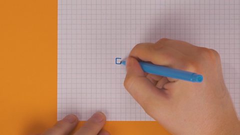 Someone drawing a square onto squared paper