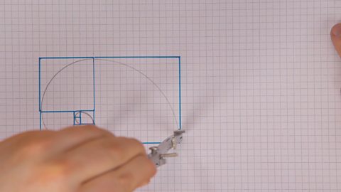 Someone using a compass to draw quarter circles in the larger squares