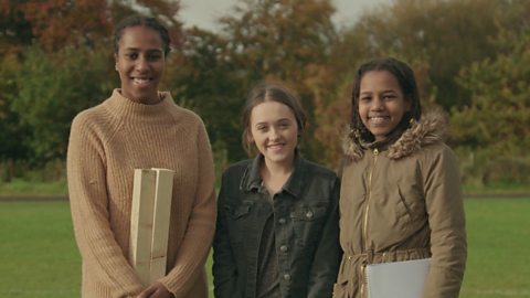 Three people standing holding two pieces of wood, a stopwatch and a pen and paper