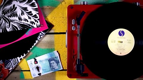 Image of a record player and a pile of vinyls surrounding a stack of £5 notes