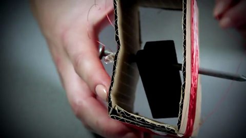 An image of the magnets either side of the nail which is pushed through the folded cardboard 