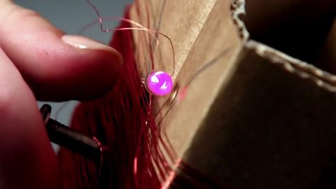 A lit up bulb which is wrapped around the copper wire on top of the folded up cardboard