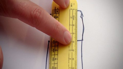 Someone using a ruler to measure the length of the original square that was traced before