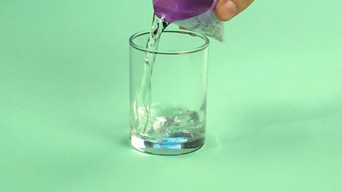 Someone pouring a cone full of water into a glass