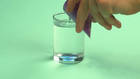 Someone pouring a cone full of water into a glass