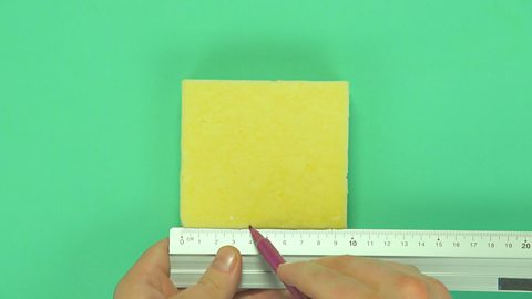 Someone placing a ruler on a block of cheese