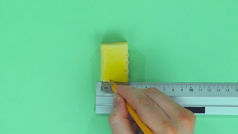 Someone marking their measurements on a block of cheese