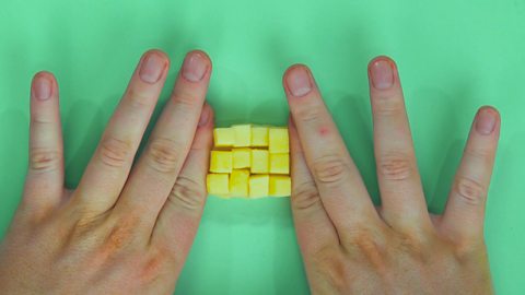 Someone holding together a diced up block of cheese