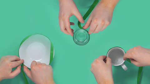 A plate, glass and a mug getting a ribbon covered around them