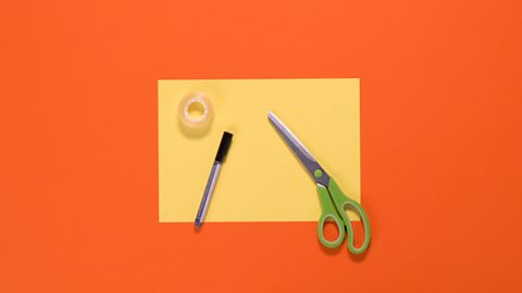 An A4 sheet of paper, scissors, sticky tape and pen are all arranged on a table.