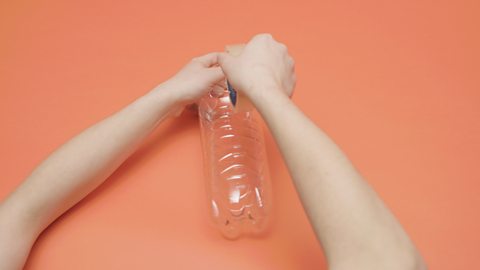 plastic bottle held by person who is covering  the holes with sticky tape.