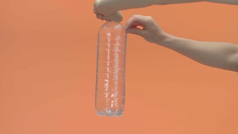 The bottle is being carried to a hold over a container they are holding the bottle upright and pulling the tape off quickly from each hole