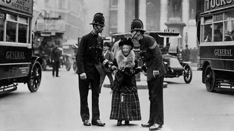 London traffic police helping an elderly lady across a busy street in the early 1900s