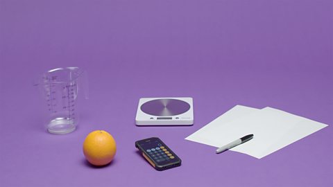 Orange, measuring jug, scales, pen, paper and calculator